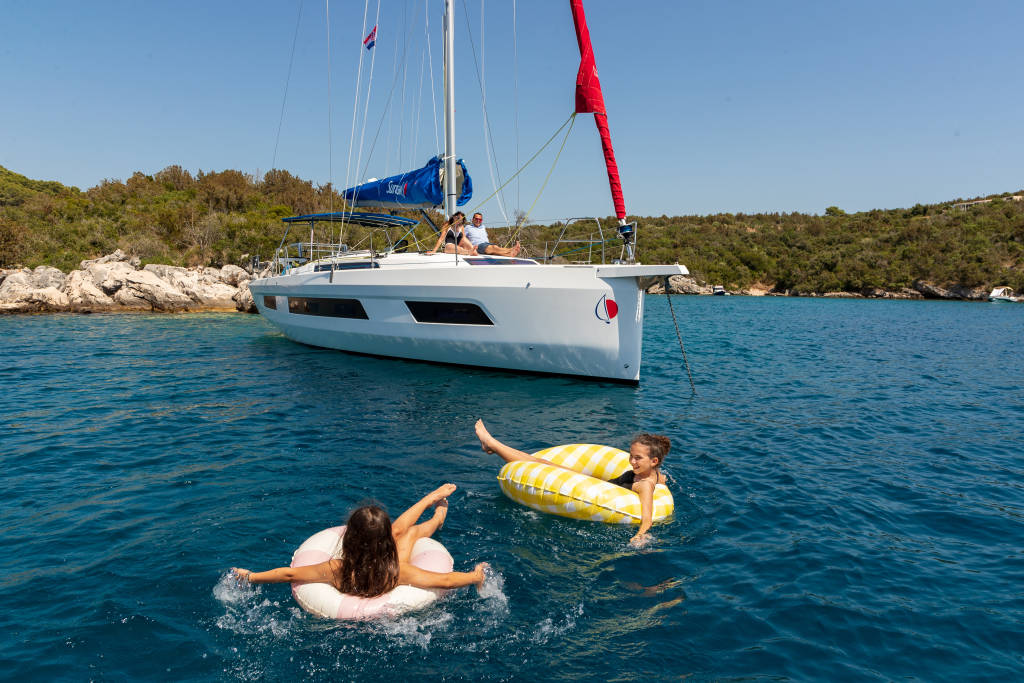 Family sailing on a yacht with kids on inflatables in the water